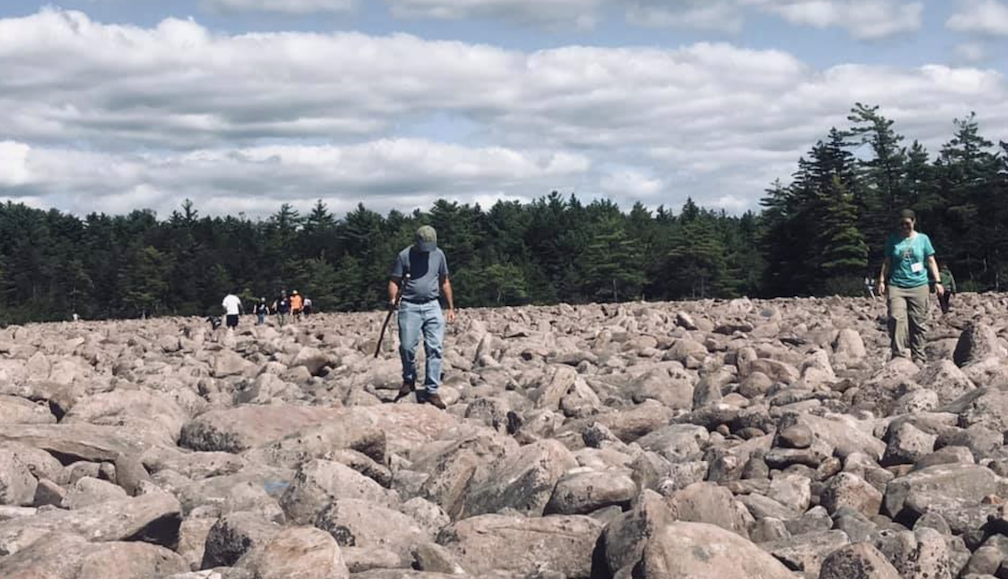 Humans walking across a field of boulders on a sunny day with white clouds in the sky