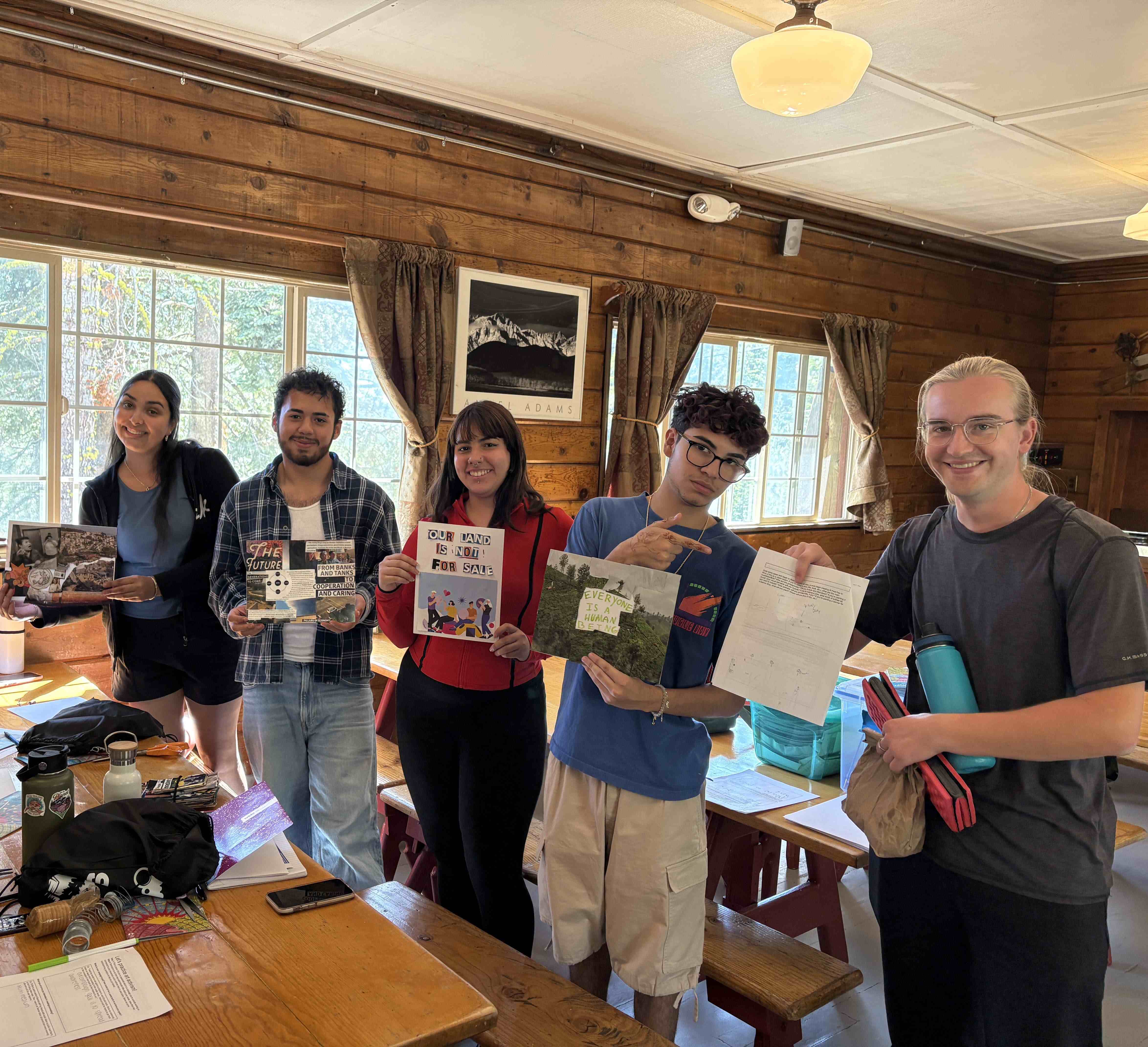 A group of 5 youth hold collages for various causes. One says "Our Land is Not for Sale, while others hold collages with folks taking action for social justice