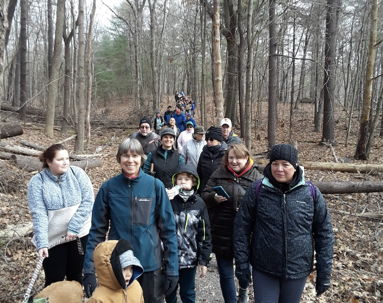 large group of bundled up hikers walking through barren woods on trail