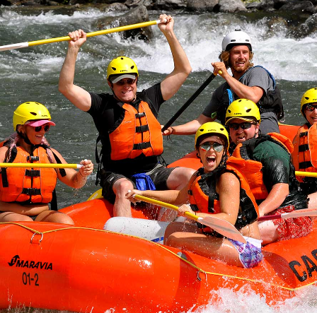 A group of 5 people sit smiling on a raft in the Payette River