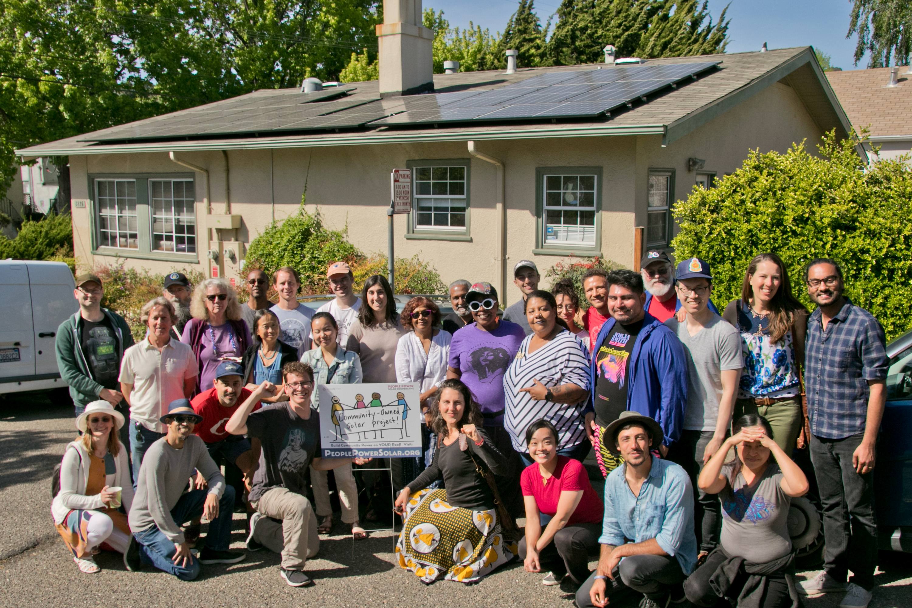 A group of neighbors stands in front of a community solar project, smiling