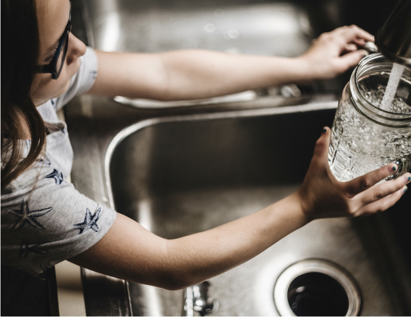 Child filling glass jar with water from a kitchen faucet